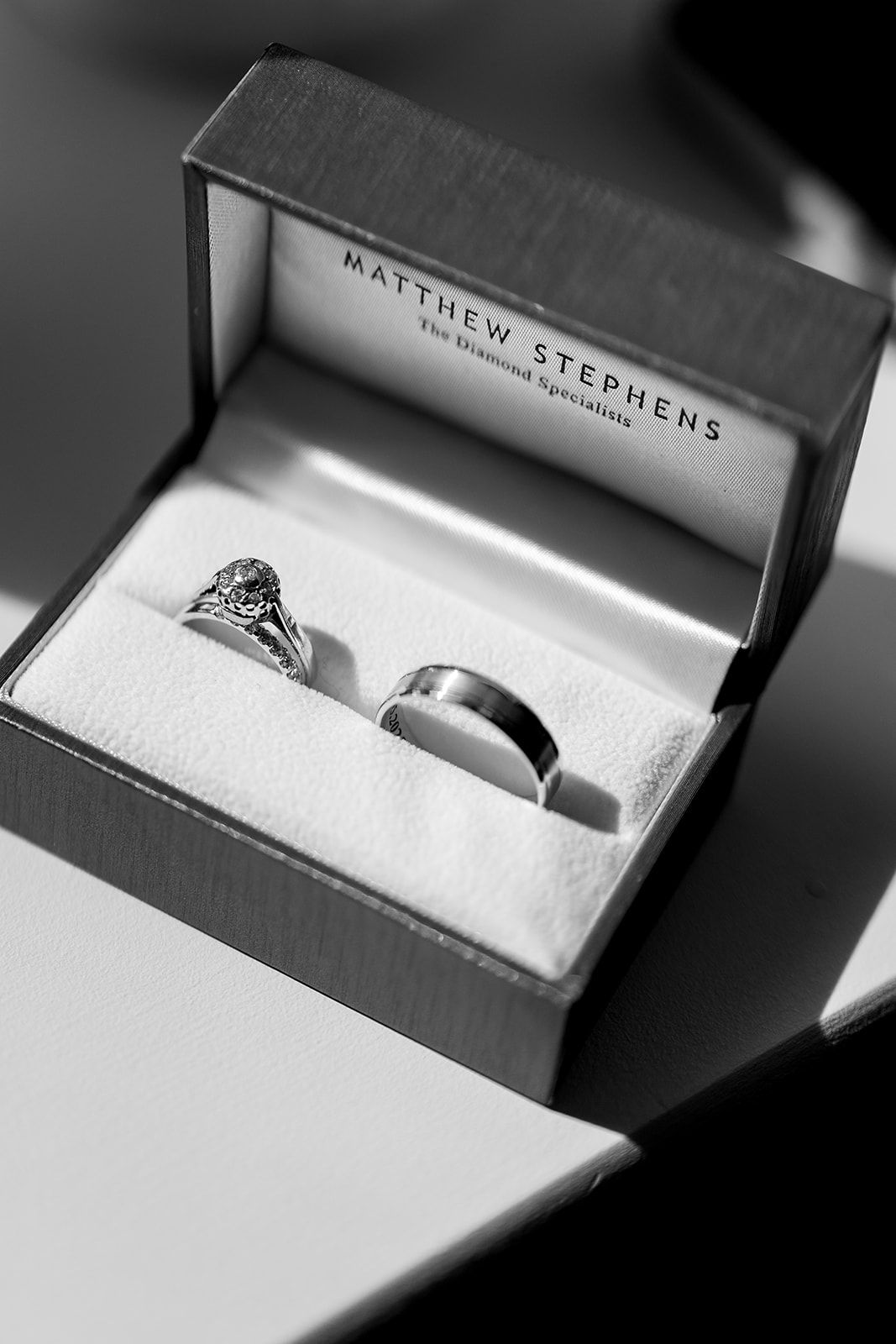 Black and white photograph of wedding rings in an elegant Matthew Stephens jewelry box.