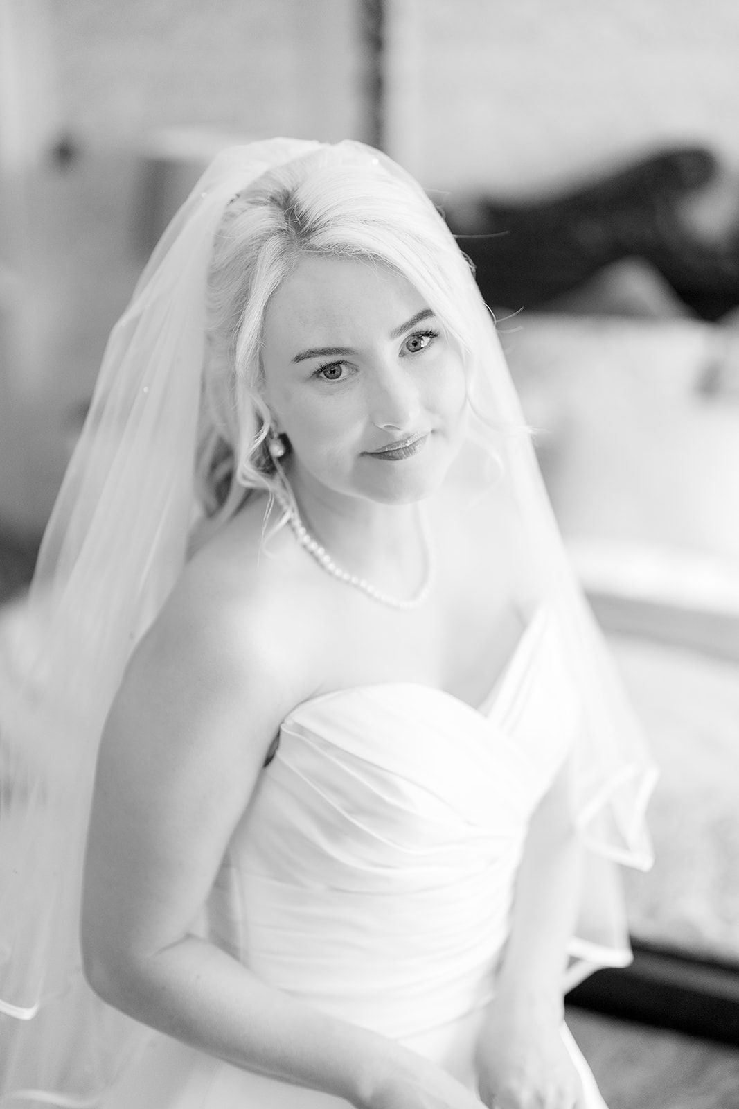 A bride in a classic white strapless wedding gown and veil smiles in this elegant black and white portrait.