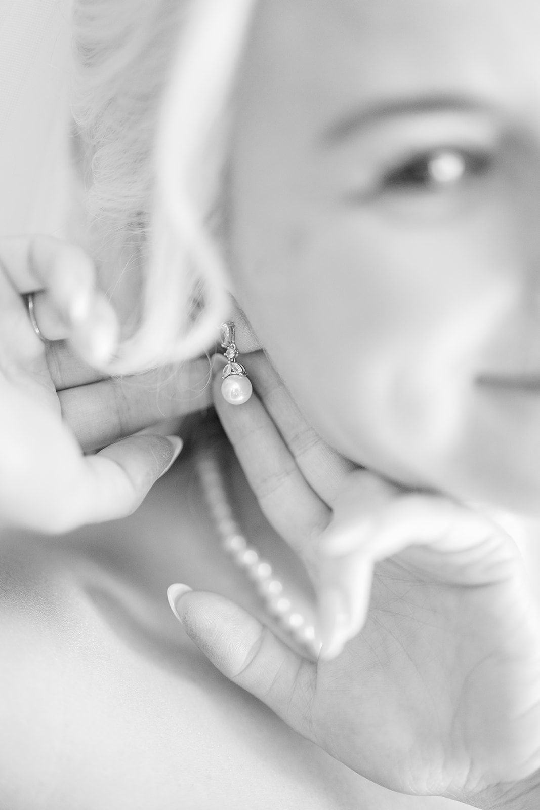 Close up black and white photo showing hands putting on a delicate pearl earring.