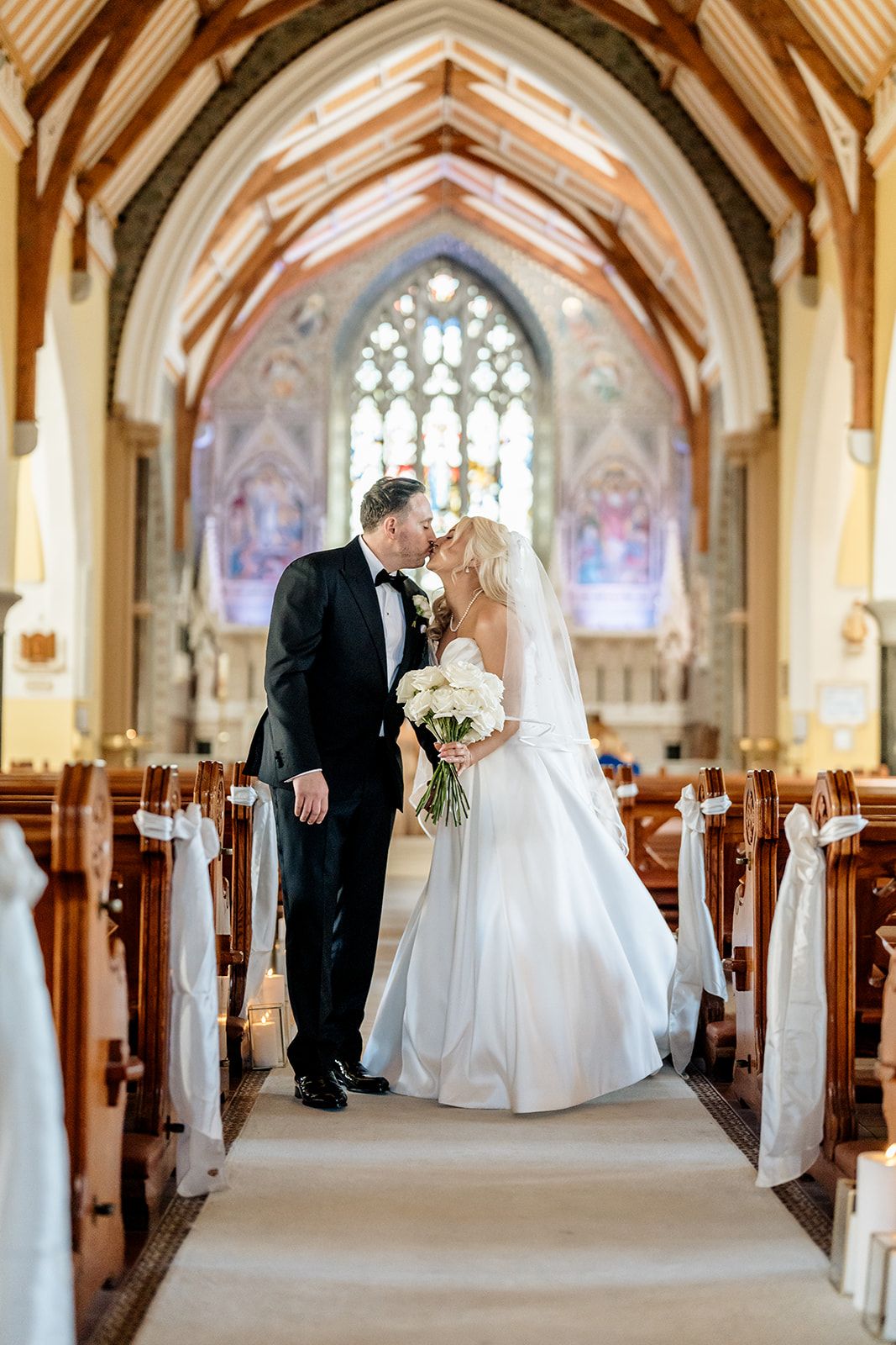 Elegant church wedding ceremony with stained glass windows and wooden beams framing the cathedral aisle.