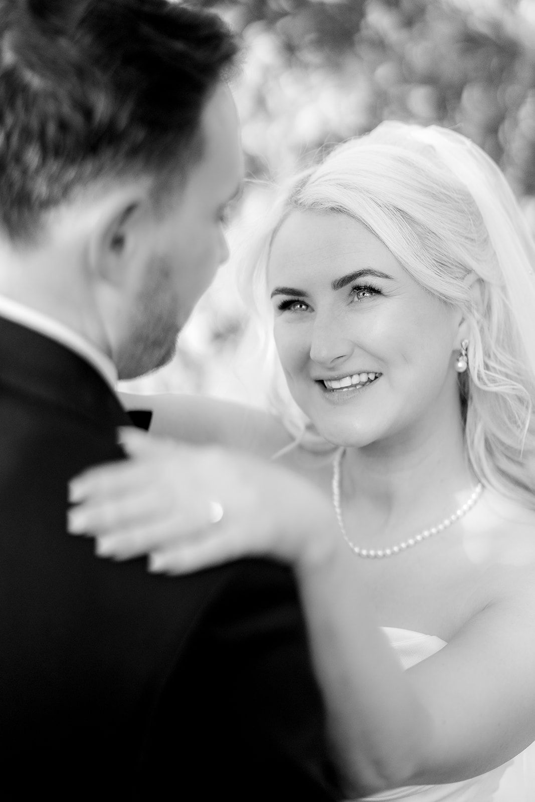 Black and white close-up portrait capturing a tender wedding moment with pearl jewelry details.