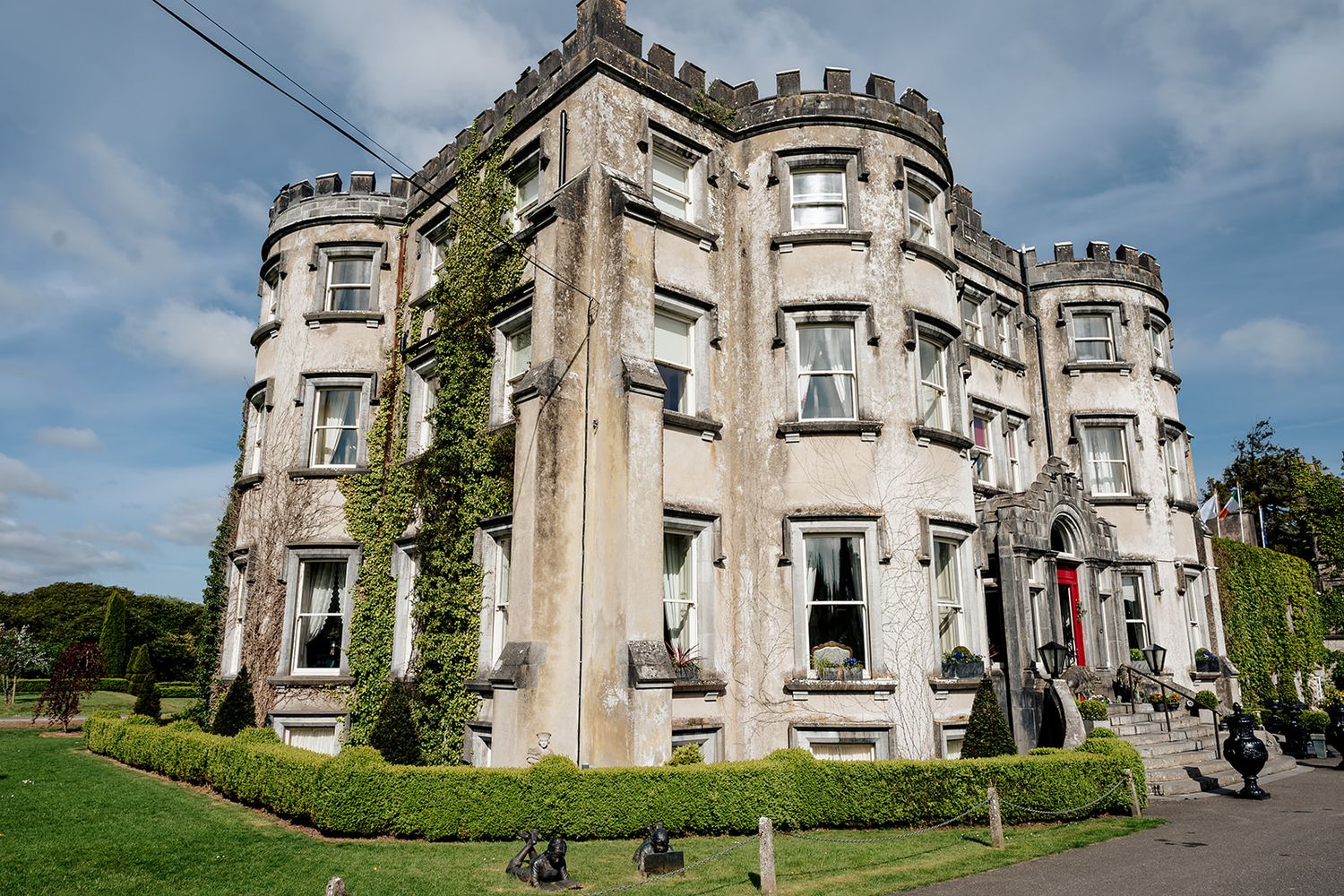 Historic stone castle with curved turret architecture and ivy-covered walls stands against blue sky at an Irish estate.