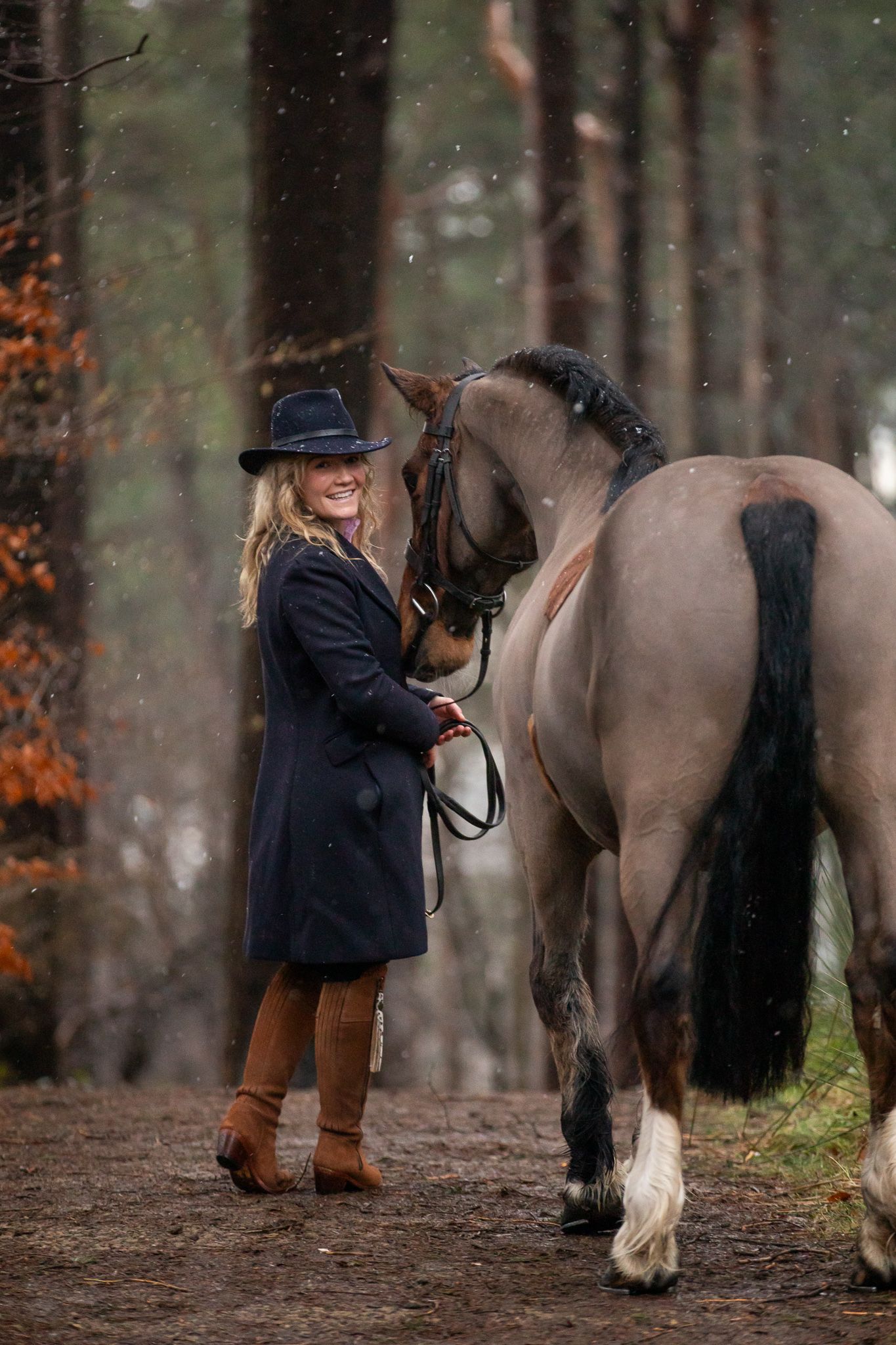 A majestic white horse stands with its handler amidst brown autumn hills during golden hour.