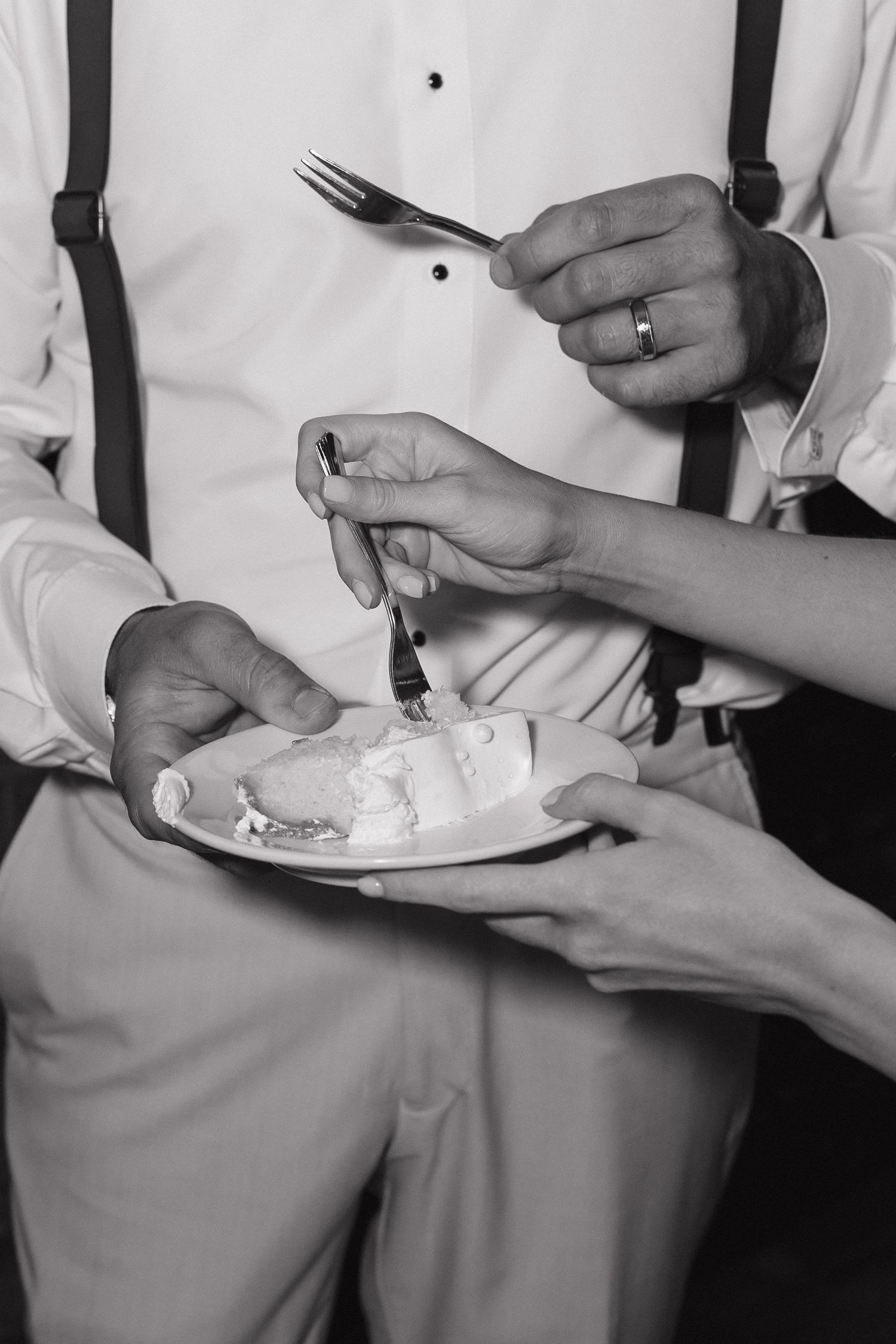 Black and white photo showing hands holding plates and utensils while eating at a dining table.