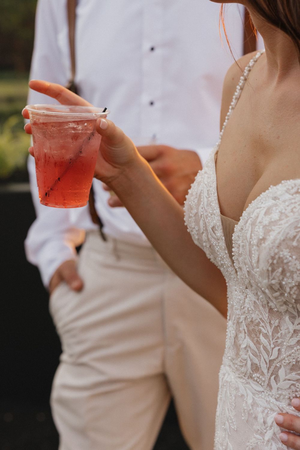 A couple in wedding attire holds red cocktails while celebrating their special day.