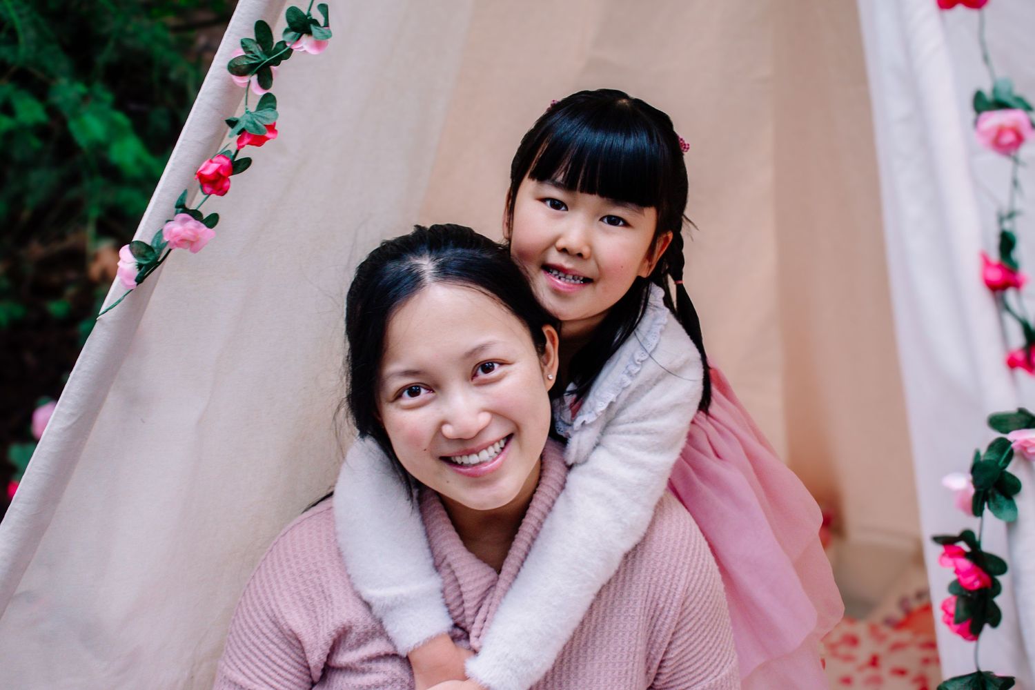 Mother and daughter snuggled under a floral teepee—joyful Mommy and Me mini session with soft spring colors.