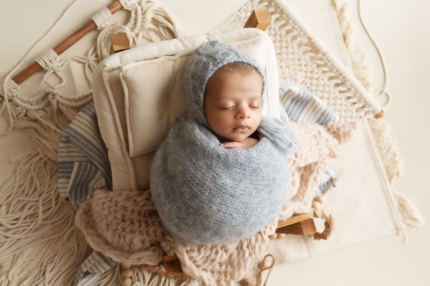 Sleeping newborn baby wrapped in soft gray swaddle on cream textured blanket with macrame decor.