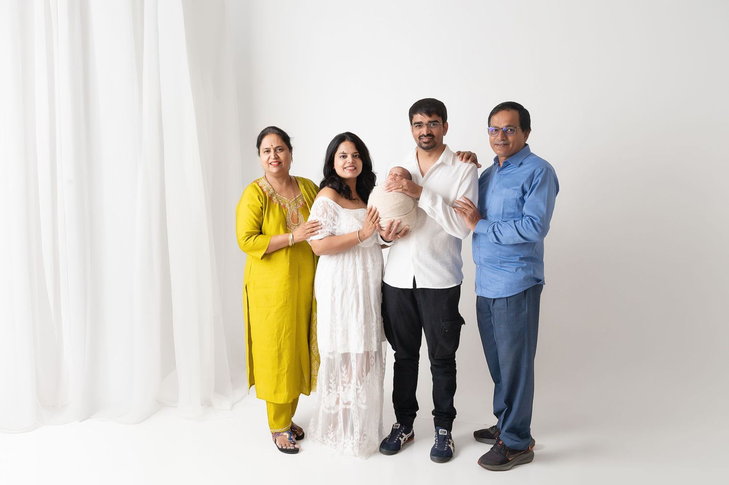 Family group portrait against white background with baby and traditional formal attire.