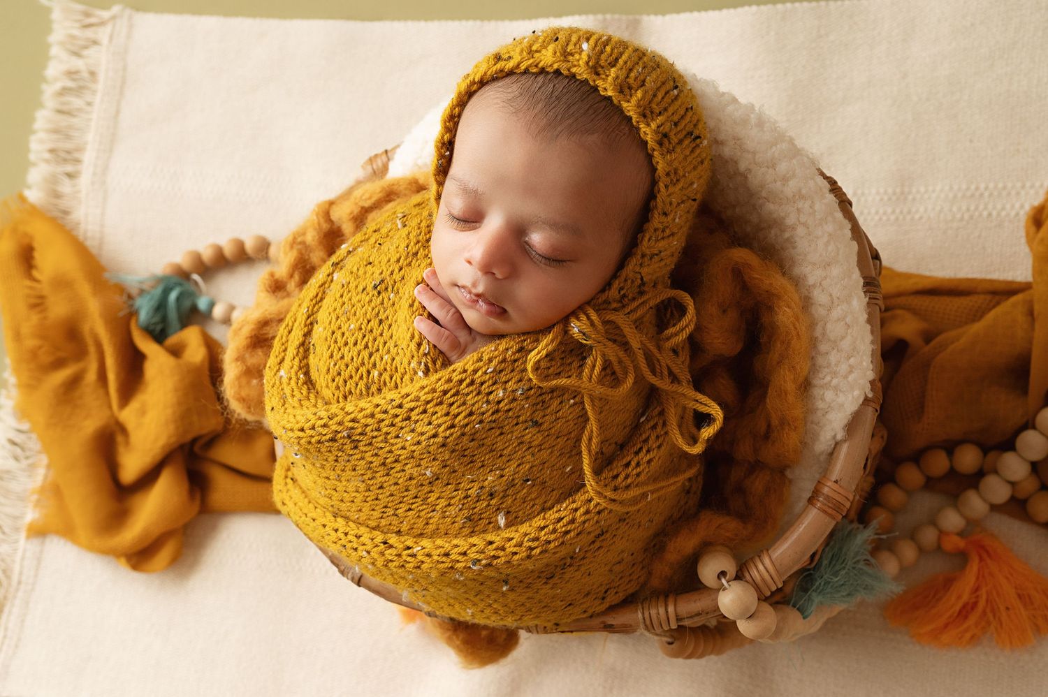 Newborn baby sleeping peacefully wrapped in cozy mustard yellow knit blankets.