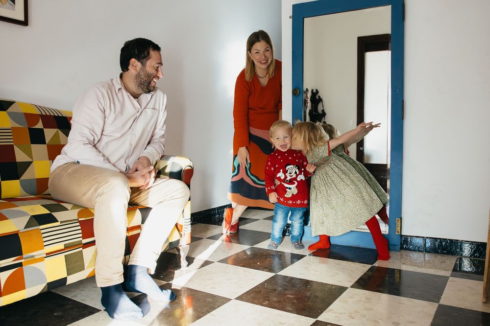 People gather in a colorful entryway with checkered floor tiles while a small child plays with a ball.