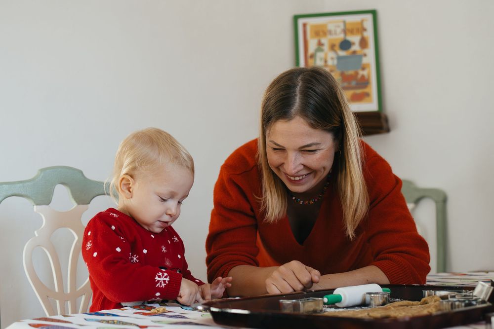 Person wearing a red sweater explores fun holiday crafts with a small child in a red sweater at a light colored table.