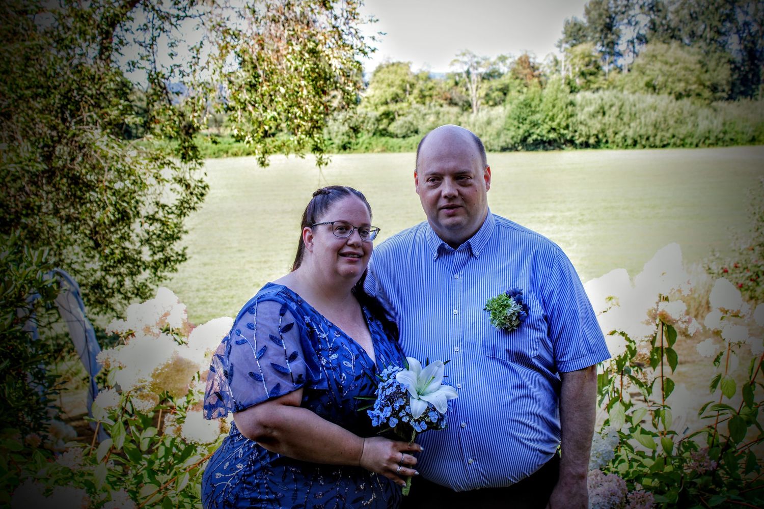 Bride in blue dress and groom in blue shirt in front of flowers and a field