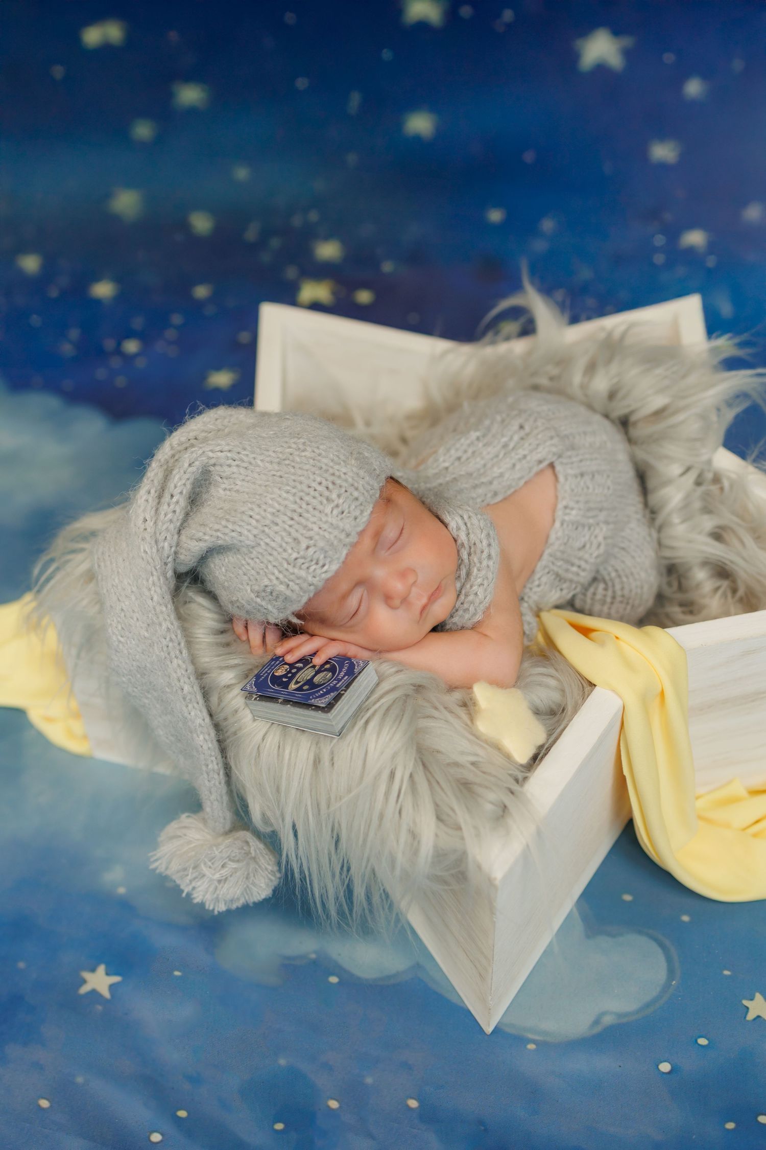 Sleeping baby in gray knit outfit lying on soft fur blanket against starry blue background with yellow accents.