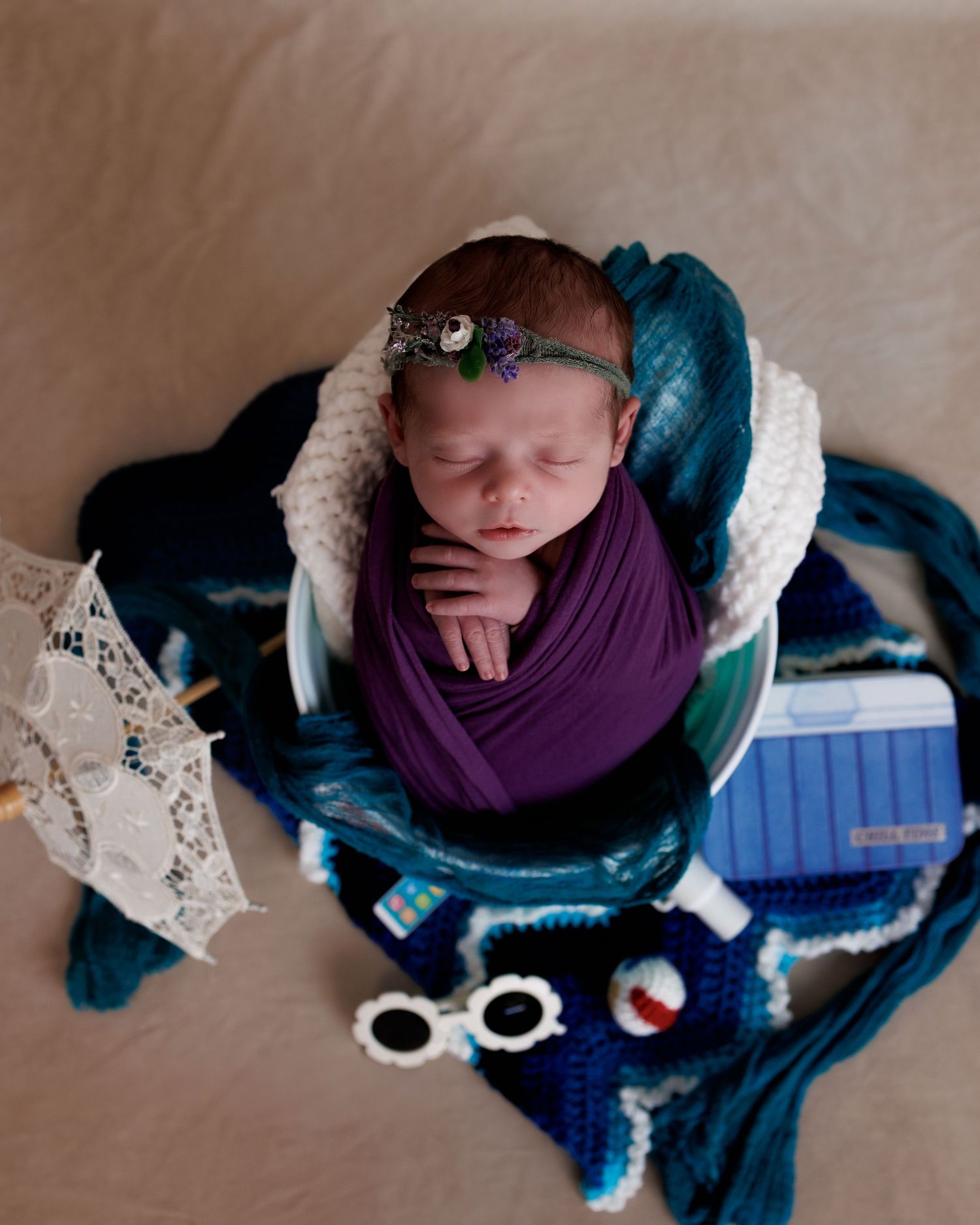 Sleeping newborn wrapped in purple swaddle on blue blanket with decorative stars and accessories for newborn photography.