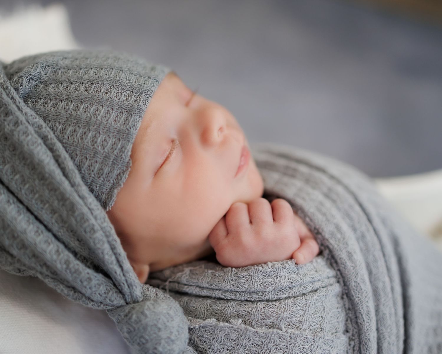 Peaceful newborn swaddled in soft gray knit fabric with matching hat.