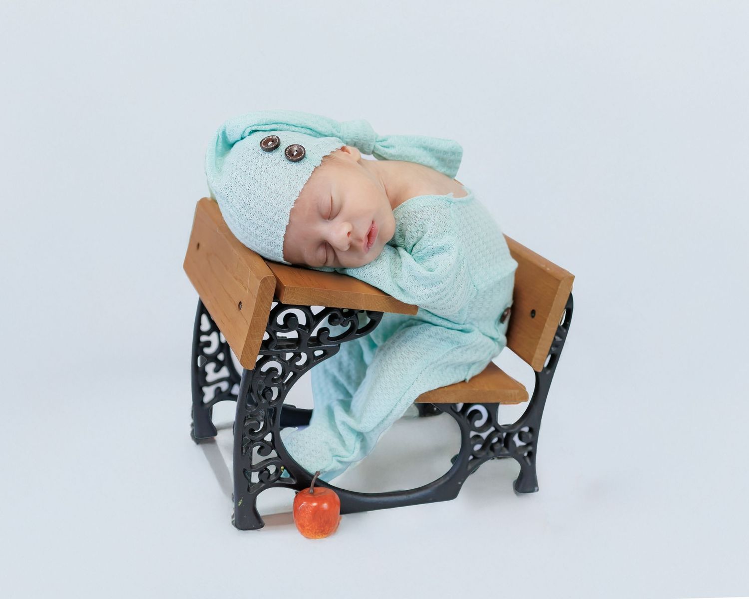 A small figure in mint green pajamas sleeps peacefully on a vintage school desk with an orange pumpkin on the floor.