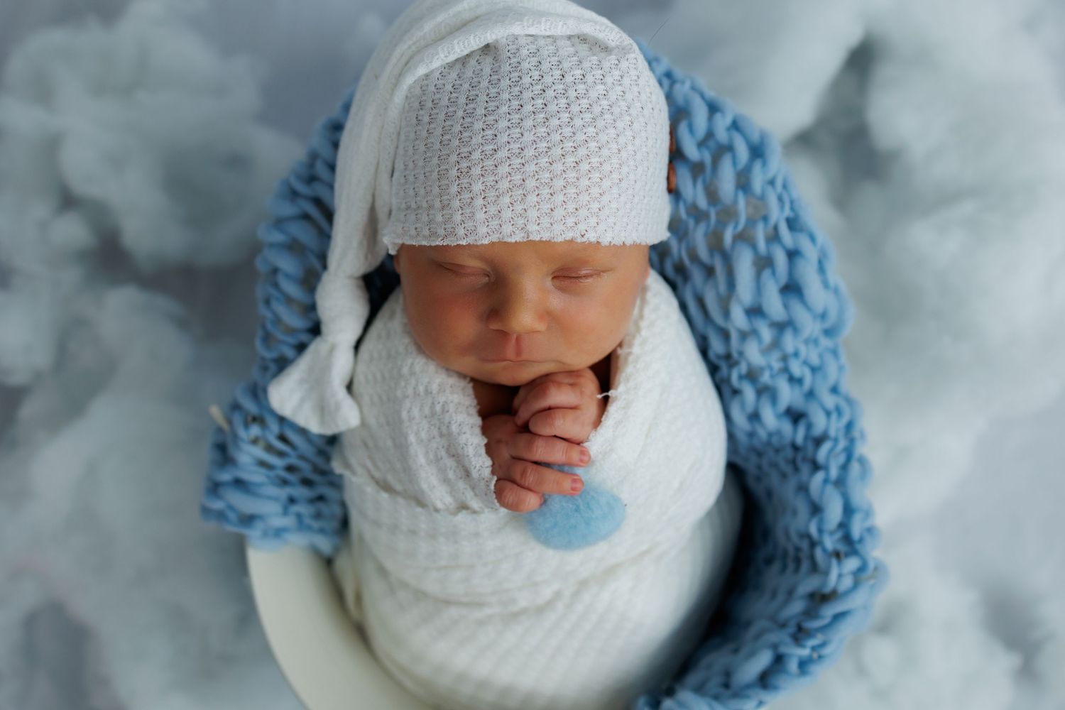 Newborn baby wearing white knit hat and blue blanket lying on soft white fabric in artistic collage style photo.