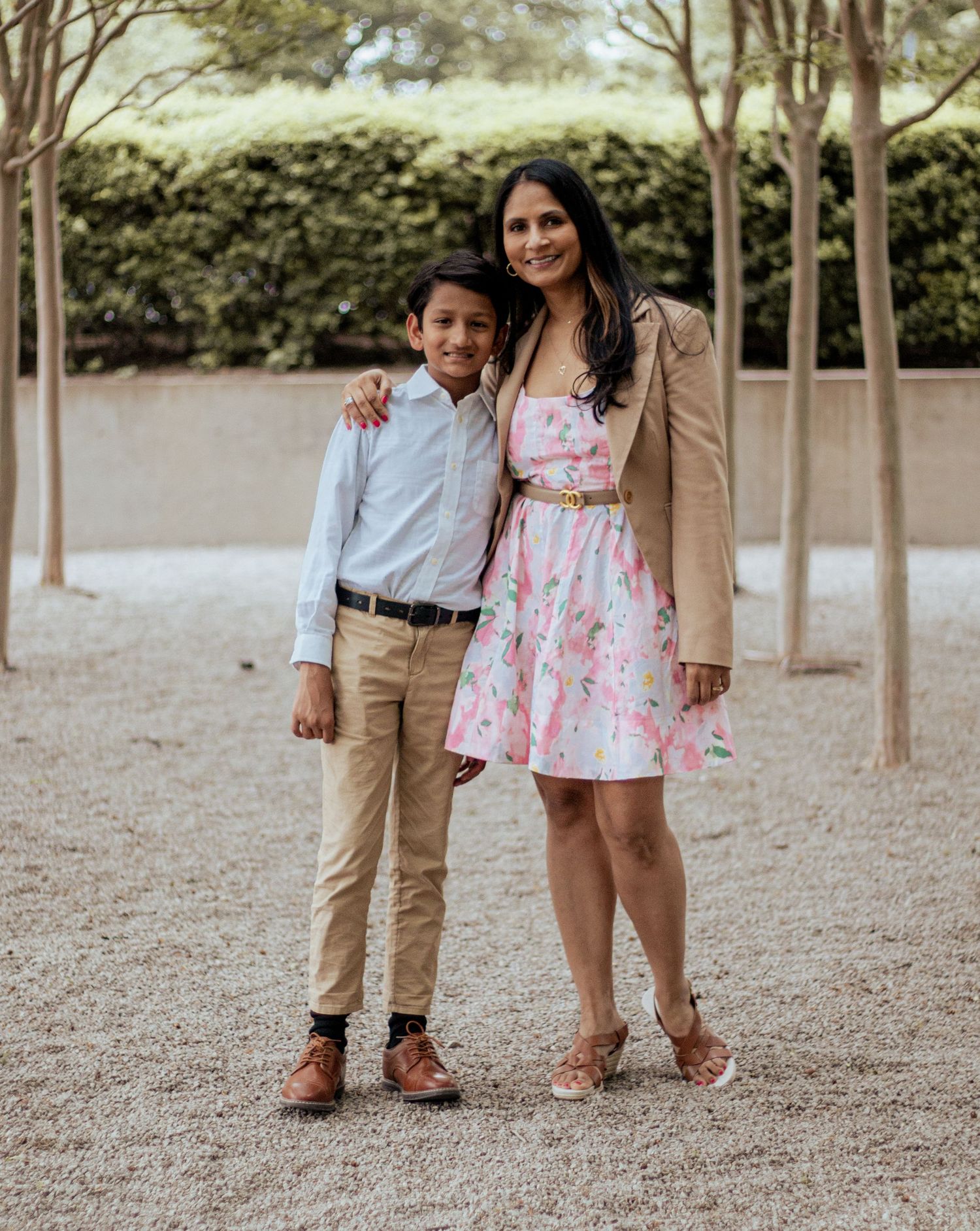 Two people in coordinated outfits standing together on gravel path with trees in background during outdoor photoshoot.
