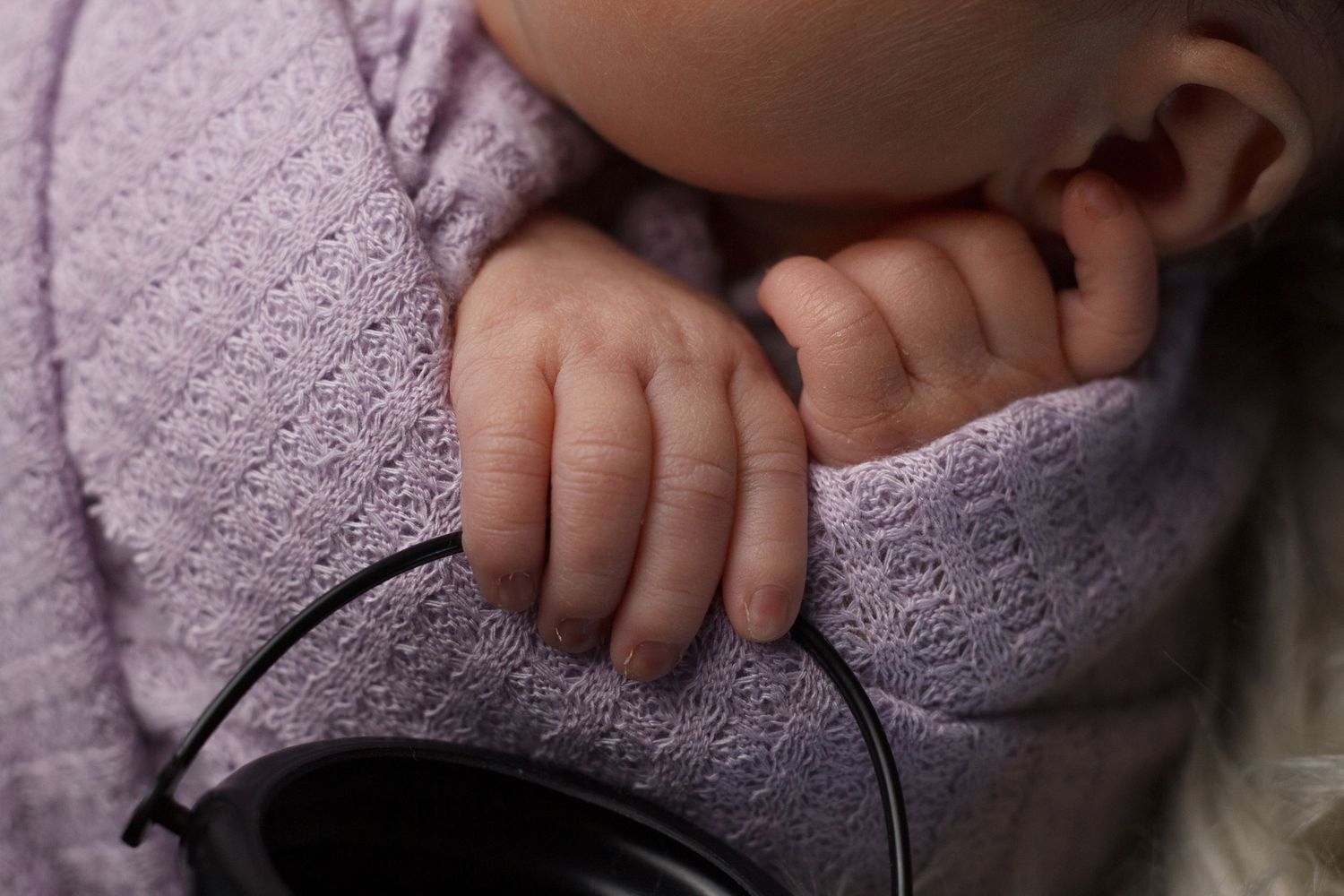 Newborn baby girl wrapped in vintage lavender wrap holding a tiny cauldron