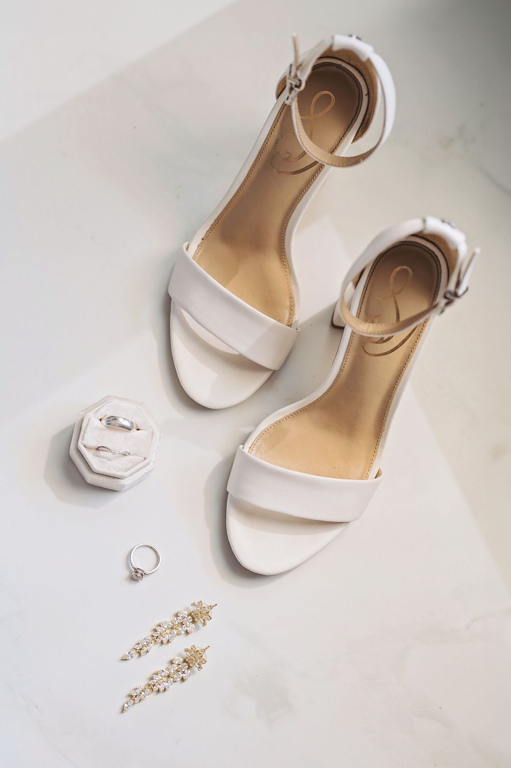 White bridal sandals with jewelry and accessories arranged on a light surface.