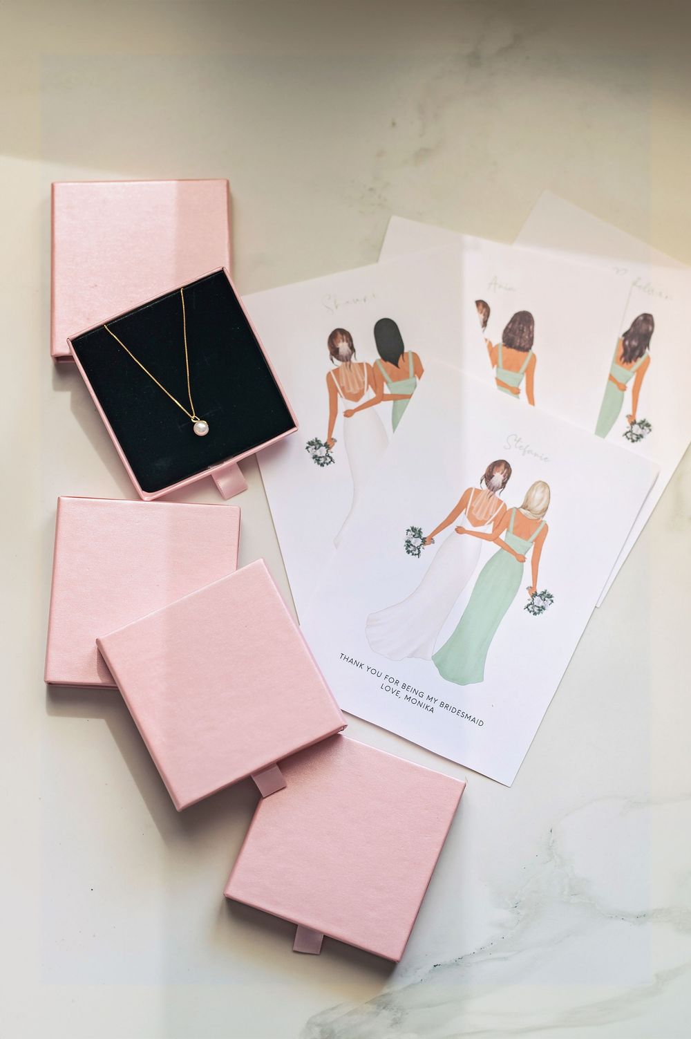 Pink gift boxes and custom illustrations displayed on a white marble surface.