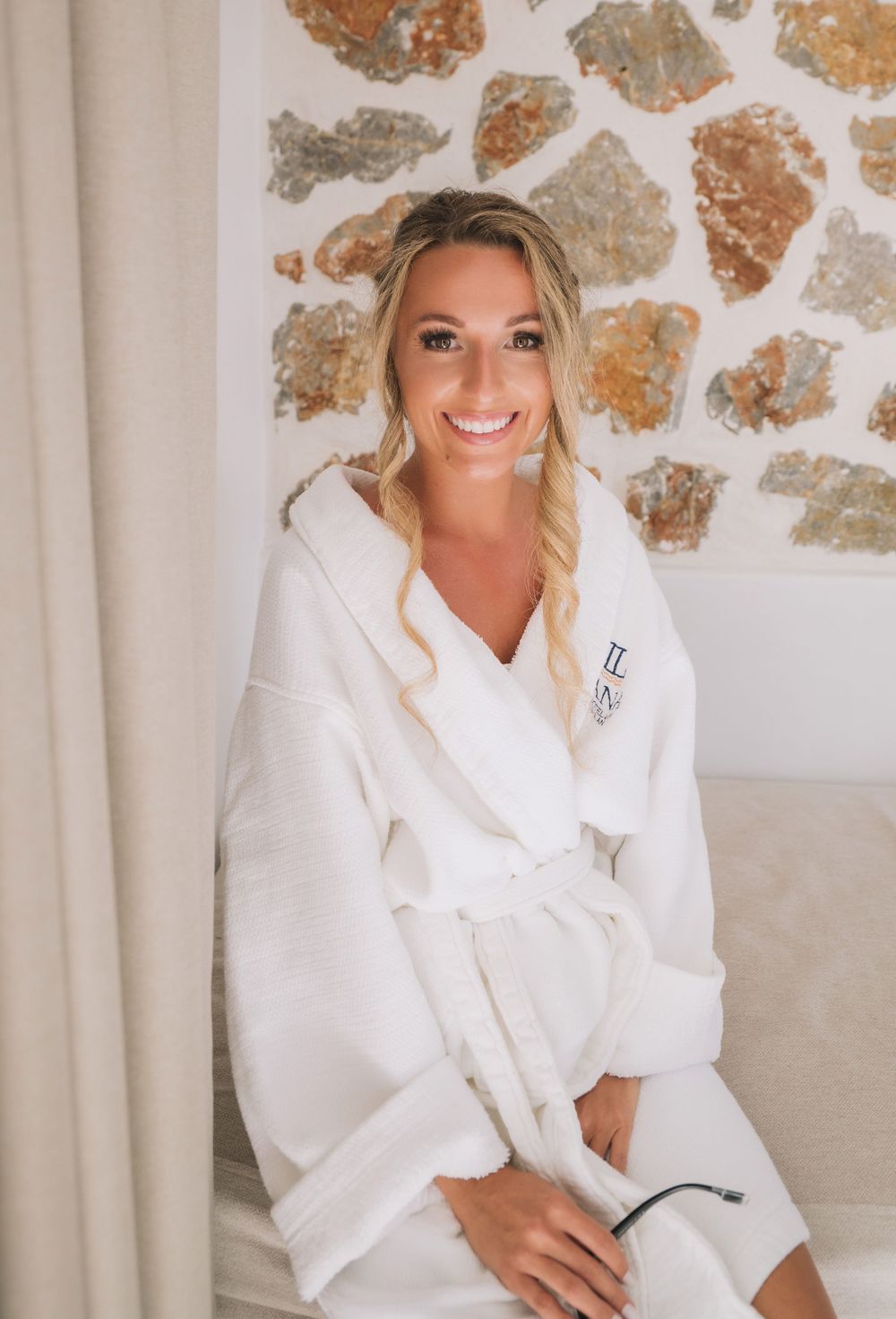 Someone wearing a white plush robe poses against a stone wall during wedding preparations.