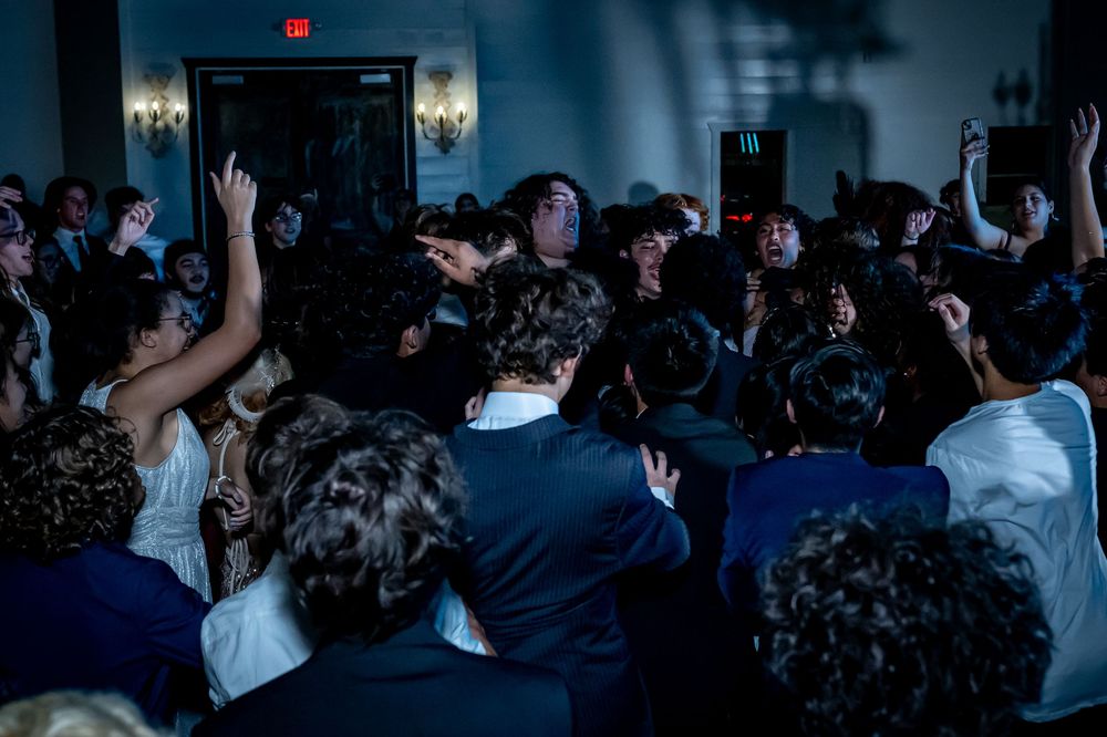 A crowded church hall filled with people raising their hands in prayer during a dimly lit service.
