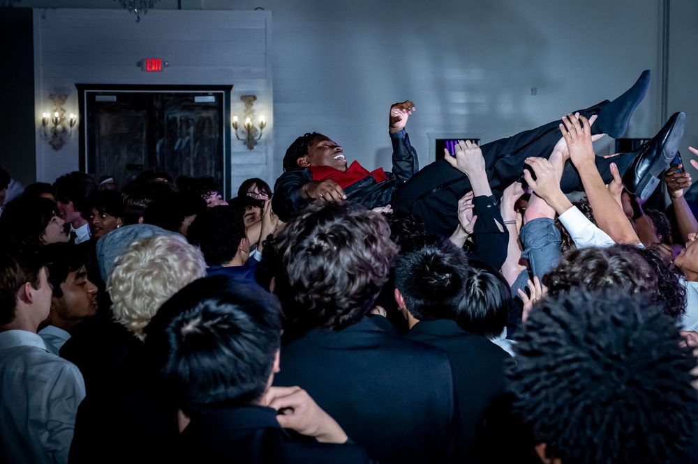 An energetic crowd at a concert venue lifts and supports a crowd surfer during a live music performance.