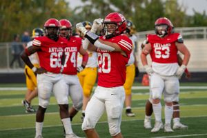 Football player in red jersey number 20 celebrates with teammates during a game on artificial turf field.