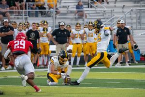 Football player in yellow uniform kicking field goal while opponent in red jersey attempts to block the attempt.