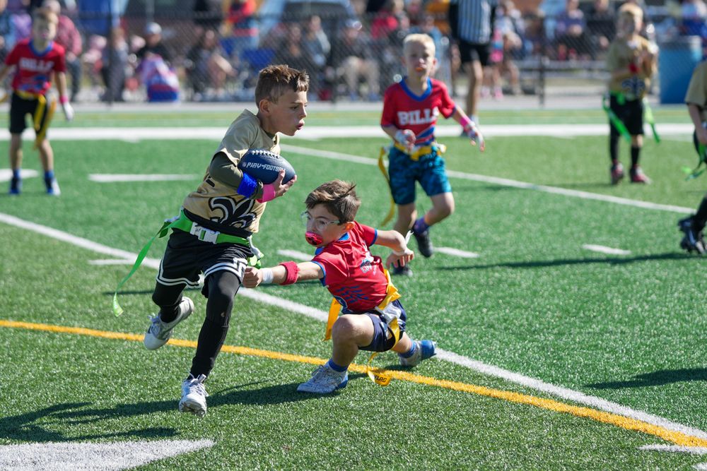 Young flag football players compete on artificial turf field during a youth sports match.