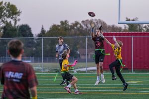 Players jump high to catch a football during a competitive game on an outdoor field at sunset.
