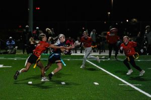 Ultimate frisbee players compete on a turf field at night under lights during an intense match.