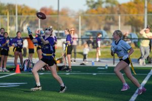A competitive flag football game on an outdoor field with players running and reaching for the ball.
