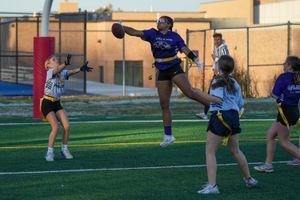 Athletes practice cheerleading jumps and stunts on an outdoor turf field during afternoon practice.
