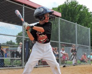 A young baseball player stands ready at bat in a batting stance wearing a black and orange uniform with white pants.