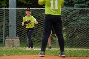 A baseball or softball player in a yellow jersey runs on a grass field during a game on a sunny day.