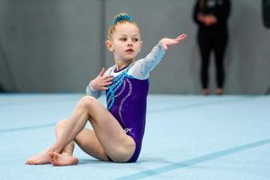 Young gymnast in purple and blue leotard performs floor routine on blue mat during competition.