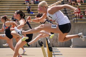 Athletes competing in a track and field hurdles race leaping over barriers on the track during competition.