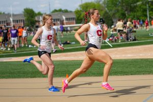 Two collegiate athletes compete in a running race on an outdoor track during a sunny spring day.