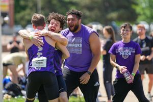 Athletic team members wearing purple shirts celebrate together during an outdoor sporting event.
