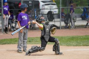Baseball catcher in protective gear crouches behind home plate during a youth baseball game.