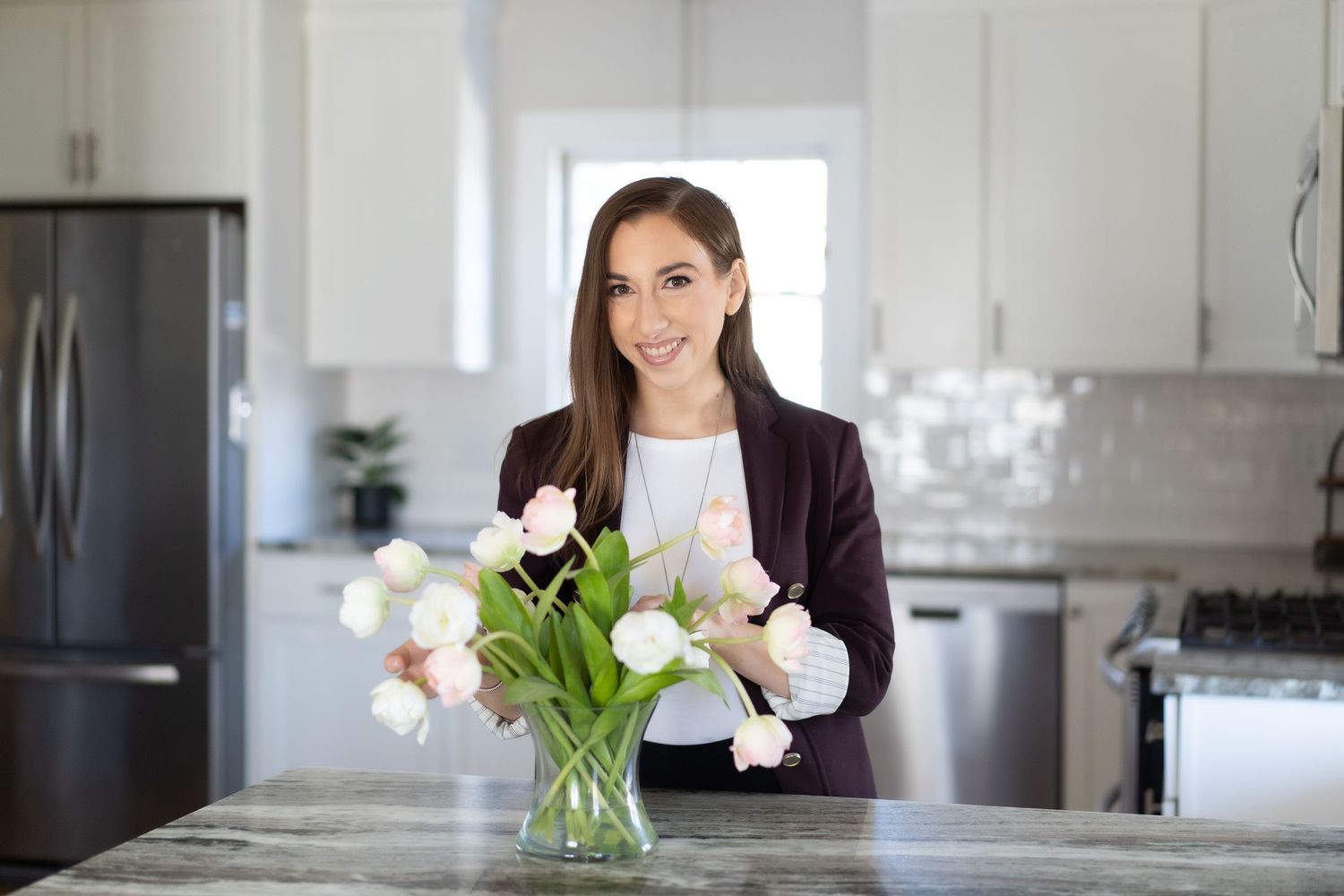 Woman arranges white tulips in glass vase on marble kitchen counter.