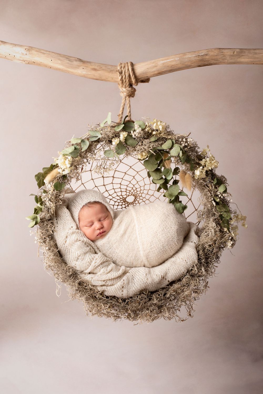 Sleeping newborn in knitted wrap nestled in dreamcatcher.