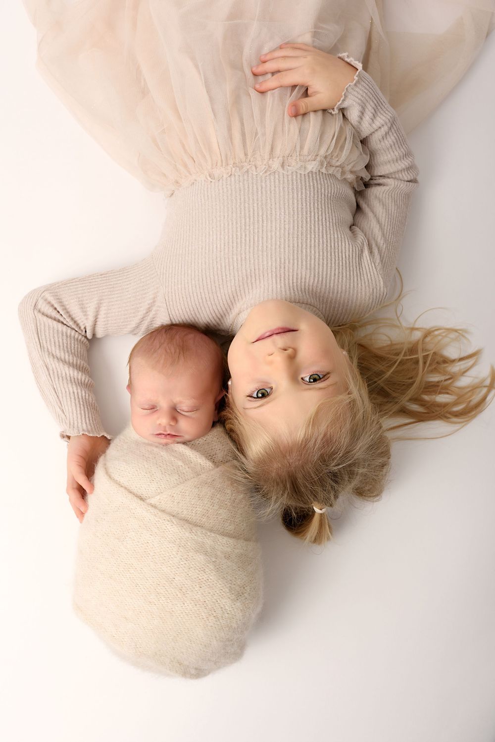 Overhead view of siblings in cream colored outfits on white background.