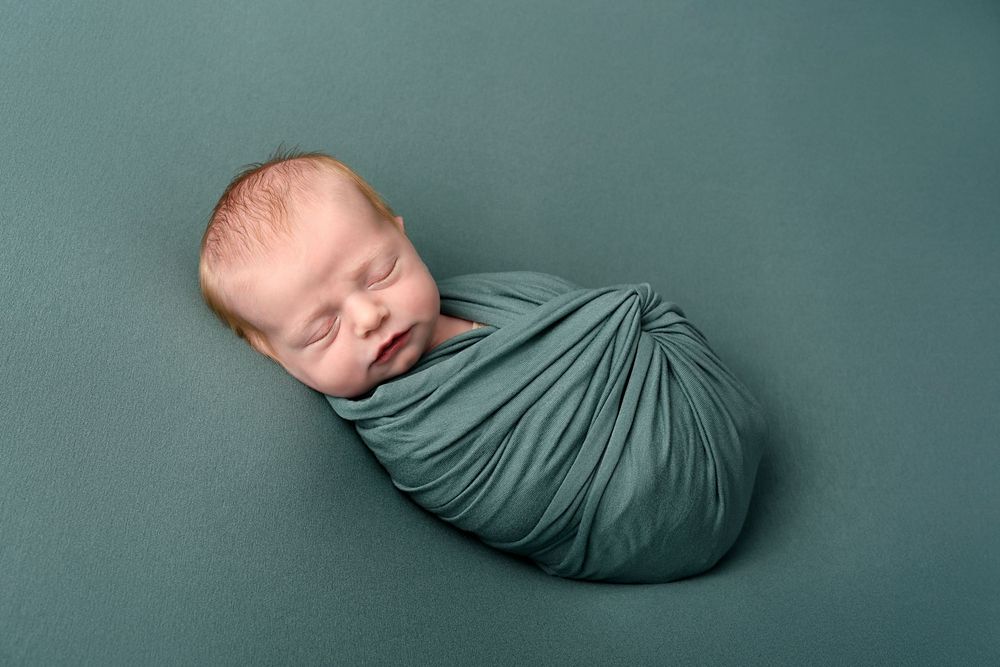 Newborn wrapped in soft sage green fabric against matching backdrop in minimalist portrait.