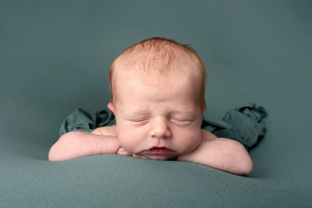 Sleeping newborn hands under chin pose against green background.