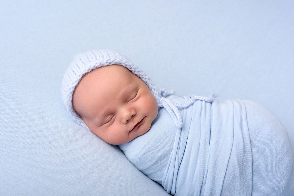 Sleeping newborn wrapped in light blue fabric wearing a bonnet.