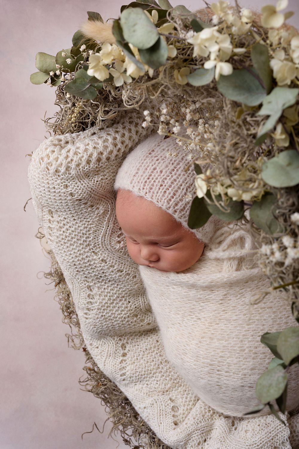 Newborn sleeping in knit wrap surrounded by dried flowers and eucalyptus.