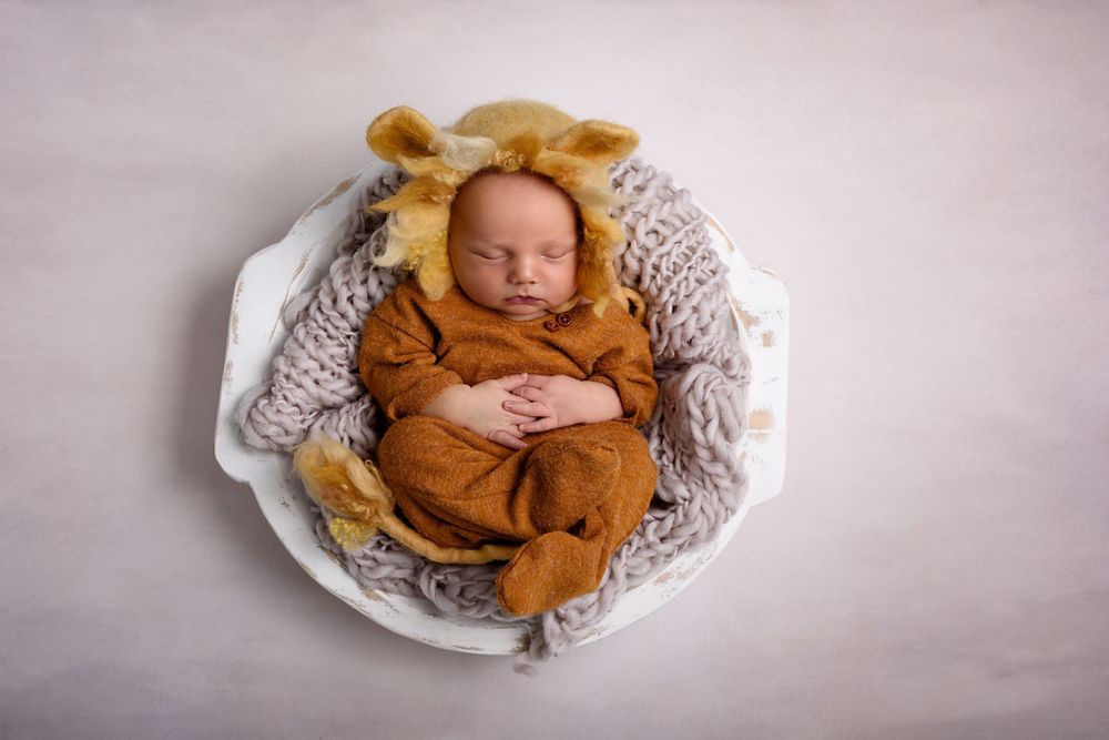 Sleeping newborn wearing lion outfit on white textured blanket.